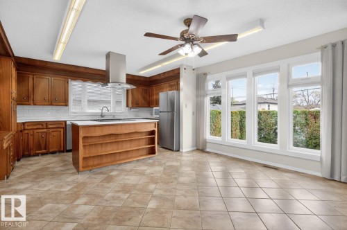 Kitchen featuring wood cabinetry, stainless steel appliances, and a central island with integrated shelving - 8911 84 Avenue, Edmonton, AB - Indoor Photo Showing Kitchen