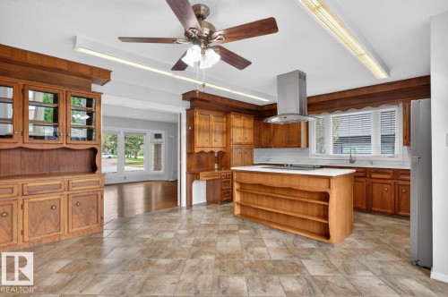 Kitchen featuring wood cabinetry, a center island with a white countertop, stainless steel range hood, stainless steel refrigerator, and tiled flooring - 8911 84 Avenue, Edmonton, AB - Indoor Photo Showing Other Room
