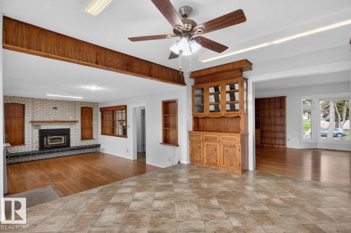 Open-concept living area with a white brick fireplace, wood-finish flooring, and a built-in wood hutch - 8911 84 Avenue, Edmonton, AB - Indoor With Fireplace