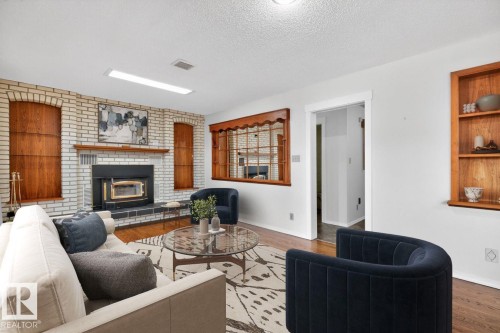 Living area featuring a white brick fireplace with a wood-burning insert, a wood mantel, and built-in wood shelving - 8911 84 Avenue, Edmonton, AB - Indoor Photo Showing Living Room With Fireplace