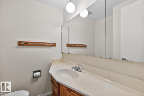 Bathroom vanity featuring a single basin sink, chrome faucet, wood cabinetry, and a large wall-mounted mirror - 8911 84 Avenue, Edmonton, AB - Indoor Photo Showing Bathroom