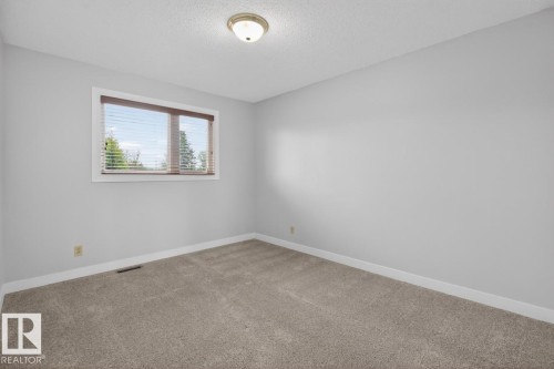 Carpeted room featuring light gray walls, a window with wood-finish blinds, and a flush-mount ceiling light fixture - 8911 84 Avenue, Edmonton, AB - Indoor Photo Showing Other Room
