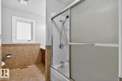 Bathroom featuring a tub/shower combination with sliding frosted glass doors, a window, and tile flooring - 8911 84 Avenue, Edmonton, AB - Indoor Photo Showing Bathroom