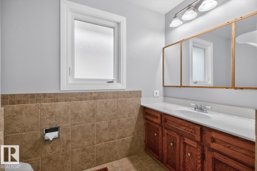 Bathroom featuring a white vanity with an integrated sink, wood-finish cabinetry, and a three-panel mirror with a wooden frame - 8911 84 Avenue, Edmonton, AB - Indoor Photo Showing Bathroom