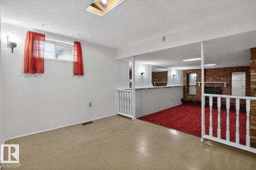 Lower-level living space featuring a window, overhead lighting, wood-finish flooring, and a brick fireplace - 8911 84 Avenue, Edmonton, AB - Indoor Photo Showing Other Room