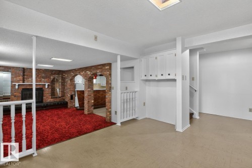 Spacious lower level featuring a brick fireplace, built-in shelving, brick archways, red carpeting, and neutral flooring - 8911 84 Avenue, Edmonton, AB - Indoor Photo Showing Other Room