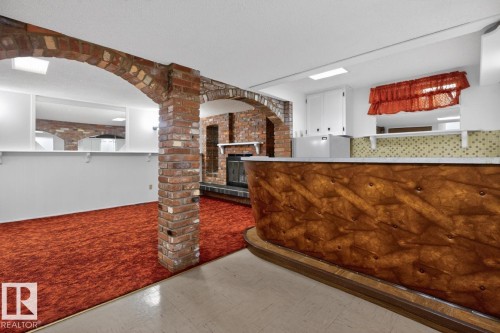 Exposed brick arches and column, built-in fireplace with brick surround, built-in bar with wood-finish paneling, white cabinetry, and recessed lighting - 8911 84 Avenue, Edmonton, AB - Indoor Photo Showing Kitchen