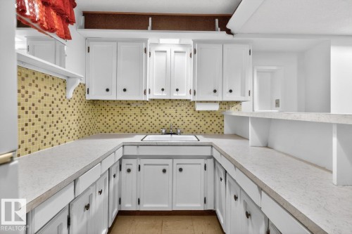 U-shaped kitchen featuring white cabinetry, light-toned countertops, a mosaic tile backsplash, and a built-in sink - 8911 84 Avenue, Edmonton, AB - Indoor Photo Showing Kitchen