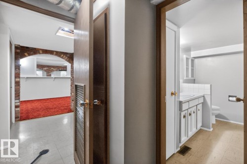 Interior hallway featuring vinyl flooring, a wood-finish door, and access to a room with brick archway detailing - 8911 84 Avenue, Edmonton, AB - Indoor