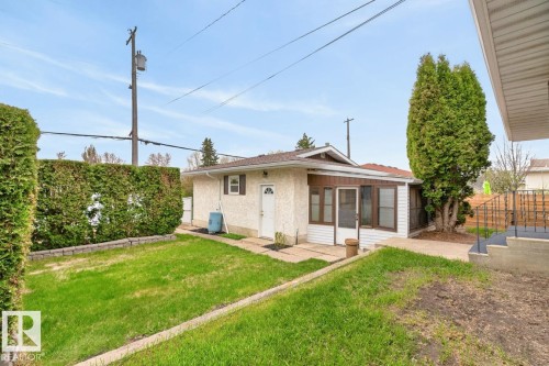 Rear exterior featuring a sunroom addition with multiple windows, stucco and siding finishes, and a paved patio area - 8911 84 Avenue, Edmonton, AB - Outdoor