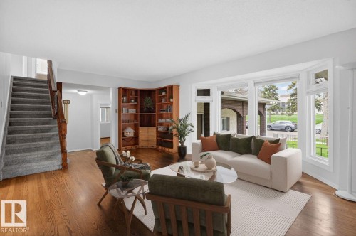 Living area featuring hardwood flooring, a large bay window, a built-in corner wooden bookshelf, a carpeted staircase with wood banister, and white wall finishes - 8911 84 Avenue, Edmonton, AB - Indoor Photo Showing Living Room