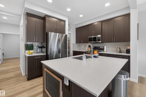 Kitchen featuring an expansive island with a light-toned countertop, dark wood-finish cabinetry, stainless steel appliances, a subway tile backsplash, and recessed lighting - 332 Juniper Cove, Leduc, AB - Indoor Photo Showing Kitchen With Upgraded Kitchen