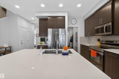 Spacious kitchen featuring a large island with an undermount sink, stainless steel appliances, dark wood-finish cabinetry, light subway tile backsplash, and recessed lighting - 332 Juniper Cove, Leduc, AB - Indoor Photo Showing Kitchen With Double Sink