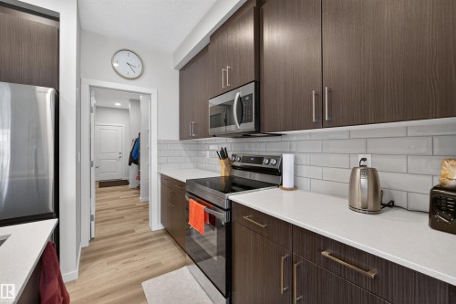 Kitchen featuring wood-finish cabinetry with modern hardware, stainless steel appliances, white subway tile backsplash, and light-toned countertops - 332 Juniper Cove, Leduc, AB - Indoor Photo Showing Kitchen With Upgraded Kitchen