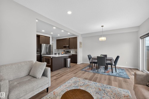 Open-concept living space featuring wood-finish flooring, recessed lighting, and a kitchen with dark cabinetry, white countertops, and stainless steel appliances - 332 Juniper Cove, Leduc, AB - Indoor Photo Showing Living Room