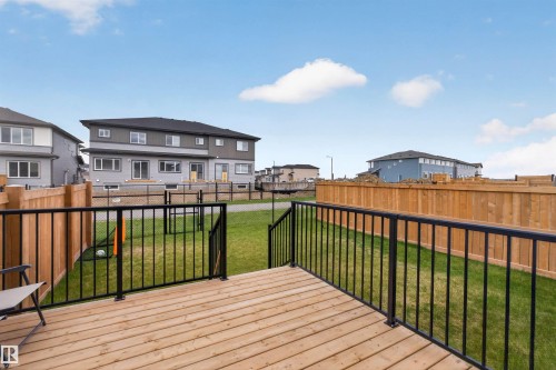 Spacious wood deck with black metal railings overlooking a backyard with green grass and a wood fence - 332 Juniper Cove, Leduc, AB - Outdoor With Deck Patio Veranda With Exterior