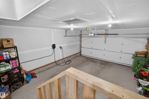 Attached garage space featuring a white sectional garage door, concrete flooring, and an electric vehicle charging station - 332 Juniper Cove, Leduc, AB - Indoor Photo Showing Garage