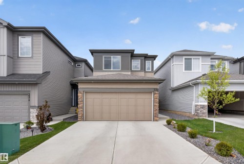 Contemporary facade featuring a two-car garage, stacked stone accents, multiple window styles, and a concrete driveway - 332 Juniper Cove, Leduc, AB - Outdoor With Facade