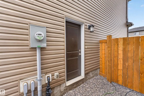 Side exterior featuring tan vinyl siding and a dark brown entry door - 332 Juniper Cove, Leduc, AB - Outdoor