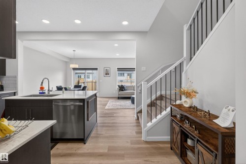 Open-concept living area featuring wood-finish flooring, recessed lighting, and a contemporary kitchen island with a stainless steel dishwasher and sink - 332 Juniper Cove, Leduc, AB - Indoor Photo Showing Kitchen With Upgraded Kitchen