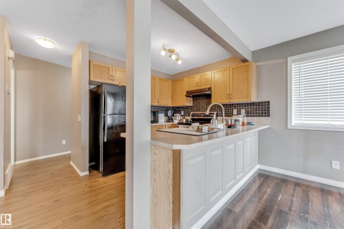 Kitchen featuring light wood cabinetry, black tiled backsplash, and a black refrigerator - 135 150 Edwards Drive, Edmonton, AB - Indoor Photo Showing Kitchen