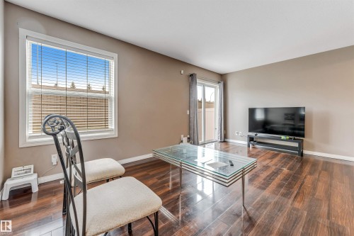Spacious living area featuring wood-finish flooring, a large window with horizontal blinds, and neutral painted walls - 135 150 Edwards Drive, Edmonton, AB - Indoor Photo Showing Living Room
