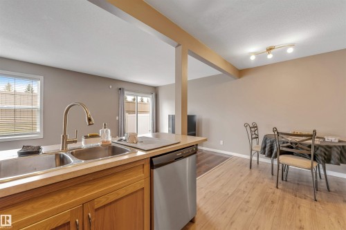 Kitchen featuring a double stainless steel sink with a high-arc faucet, light wood-finish cabinetry, and a built-in dishwasher - 135 150 Edwards Drive, Edmonton, AB - Indoor Photo Showing Kitchen With Double Sink
