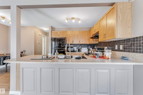 Kitchen featuring light wood-finish cabinetry, a black appliance suite, and a tiled backsplash - 135 150 Edwards Drive, Edmonton, AB - Indoor Photo Showing Kitchen With Double Sink
