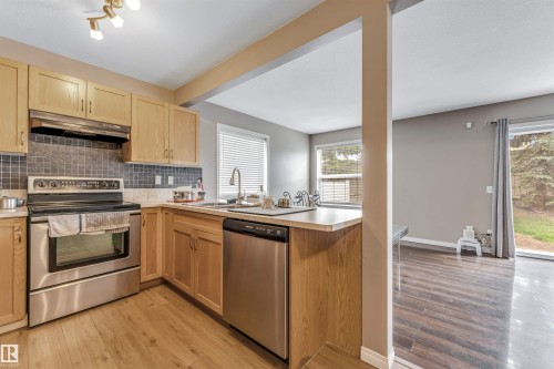 Kitchen with wood-finish flooring, light wood cabinetry, and stainless steel appliances including a range and dishwasher - 135 150 Edwards Drive, Edmonton, AB - Indoor Photo Showing Kitchen