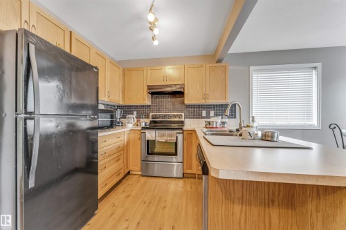 Kitchen featuring light wood cabinetry, stainless steel appliances, a tile backsplash, and light-toned countertops - 135 150 Edwards Drive, Edmonton, AB - Indoor Photo Showing Kitchen With Double Sink