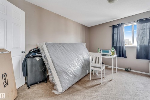 Carpeted room featuring a white interior door with a silver knob, a double-paned window, and light neutral wall paint - 135 150 Edwards Drive, Edmonton, AB - Indoor Photo Showing Bedroom