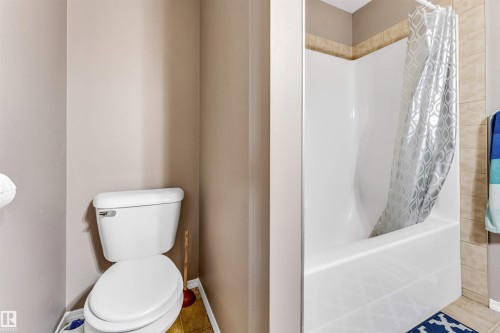White porcelain toilet and a shower-over-tub combination with light-toned wall tile accents - 135 150 Edwards Drive, Edmonton, AB - Indoor Photo Showing Bathroom