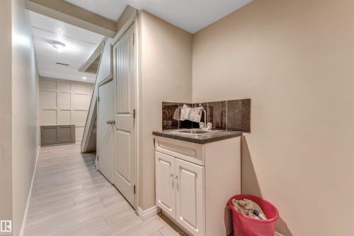 Utility sink with a dark countertop and backsplash, white cabinetry, and light-toned flooring - 135 150 Edwards Drive, Edmonton, AB - Indoor Photo Showing Other Room