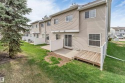 Rear exterior featuring beige siding, multiple windows, a sliding glass door, a ground-level concrete patio, and a wooden deck - 