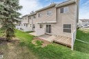 Rear exterior featuring beige siding, multiple windows, a sliding glass door, a ground-level concrete patio, and a wooden deck - 135 150 Edwards Drive, Edmonton, AB  - Outdoor With Exterior 