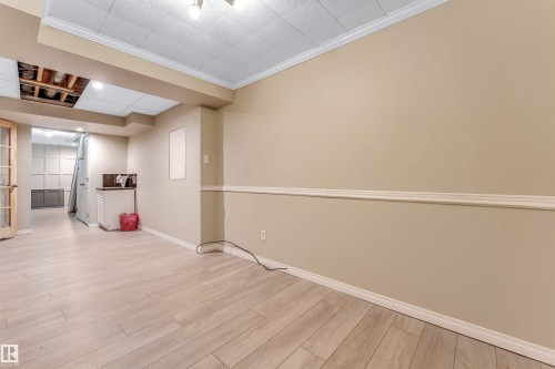 Spacious room featuring wood-finish flooring, neutral-toned walls with chair rail molding, and a drop ceiling - 135 150 Edwards Drive, Edmonton, AB - Indoor