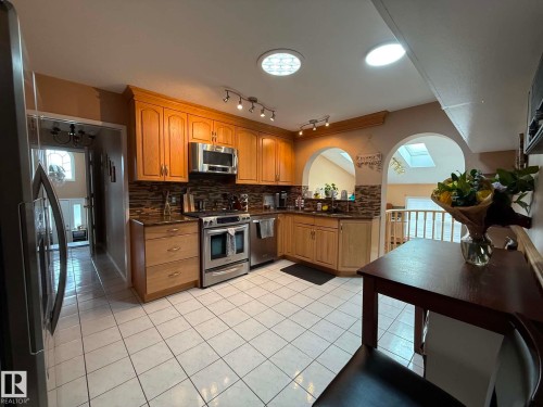 Kitchen featuring light wood-finish cabinetry, stainless steel appliances, a mosaic tile backsplash, and white square tile flooring - 2812 35 Street, Edmonton, AB - Indoor Photo Showing Kitchen