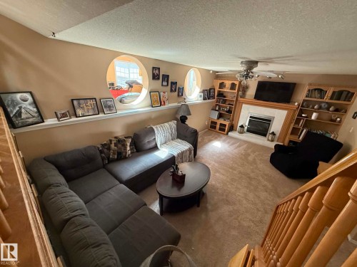 Carpeted living space featuring a fireplace with a white mantel, built-in shelving, two round window openings, and a ceiling fan - 2812 35 Street, Edmonton, AB - Indoor Photo Showing Living Room With Fireplace