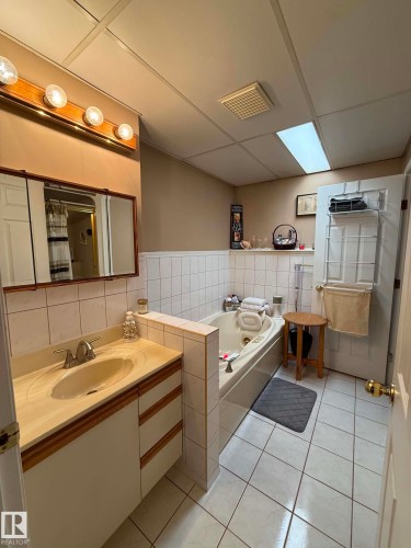 Bathroom featuring a vanity with an integrated sink and light-colored countertop, a jetted tub, and white square floor tiles - 2812 35 Street, Edmonton, AB - Indoor Photo Showing Bathroom