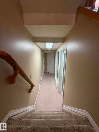Carpeted stairway with a wooden handrail, leading to a hallway featuring recessed lighting and white trim - 2812 35 Street, Edmonton, AB - Indoor Photo Showing Other Room