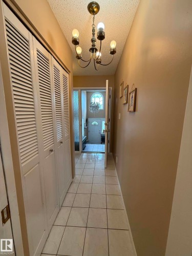 Hallway featuring a brass chandelier, tile flooring, and louvered closet doors - 2812 35 Street, Edmonton, AB - Indoor Photo Showing Other Room