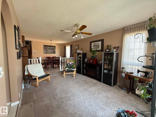 Carpeted living area featuring neutral-toned walls, a ceiling fan with light fixture, and a large window with vertical blinds - 2812 35 Street, Edmonton, AB - Indoor