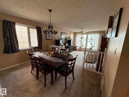Carpeted dining area featuring a dark-toned chandelier, large windows with white trim, and a white railing overlooking a lower level - 2812 35 Street, Edmonton, AB - Indoor Photo Showing Dining Room