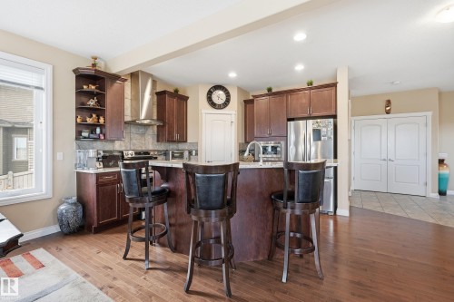 Kitchen featuring wood-finish flooring, dark wood cabinetry, stainless steel appliances, a stone tile backsplash, and a central island with a light-colored countertop - 1590 Chapman Way, Edmonton, AB 