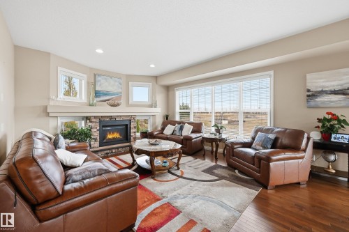 Living area featuring a stone-clad fireplace with a hearth, multiple windows, recessed lighting, and wood-finish flooring - 1590 Chapman Way, Edmonton, AB 