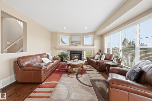 Spacious living area featuring a stone-surround fireplace, large bay windows, wood-finish flooring, recessed lighting, and a partial wall opening to a staircase - 1590 Chapman Way, Edmonton, AB 