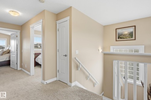 Carpeted hallway featuring white trim and doors, two open doorways, a closed door, and a staircase with white railings - 1590 Chapman Way, Edmonton, AB 