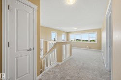 Spacious upper-level landing featuring light beige carpeting, multiple large windows, white baluster railing, and recessed ceiling lighting - 