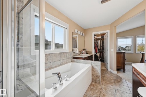 Spacious bathroom featuring a built-in soaking tub, a separate glass-enclosed shower, a double vanity with a mirror, and tiled flooring - 1590 Chapman Way, Edmonton, AB 