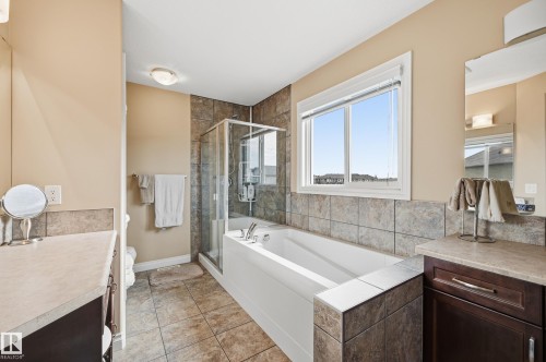 Bathroom featuring a tiled soaking tub, separate glass-enclosed shower, light-toned wall tile, and a single window - 1590 Chapman Way, Edmonton, AB 